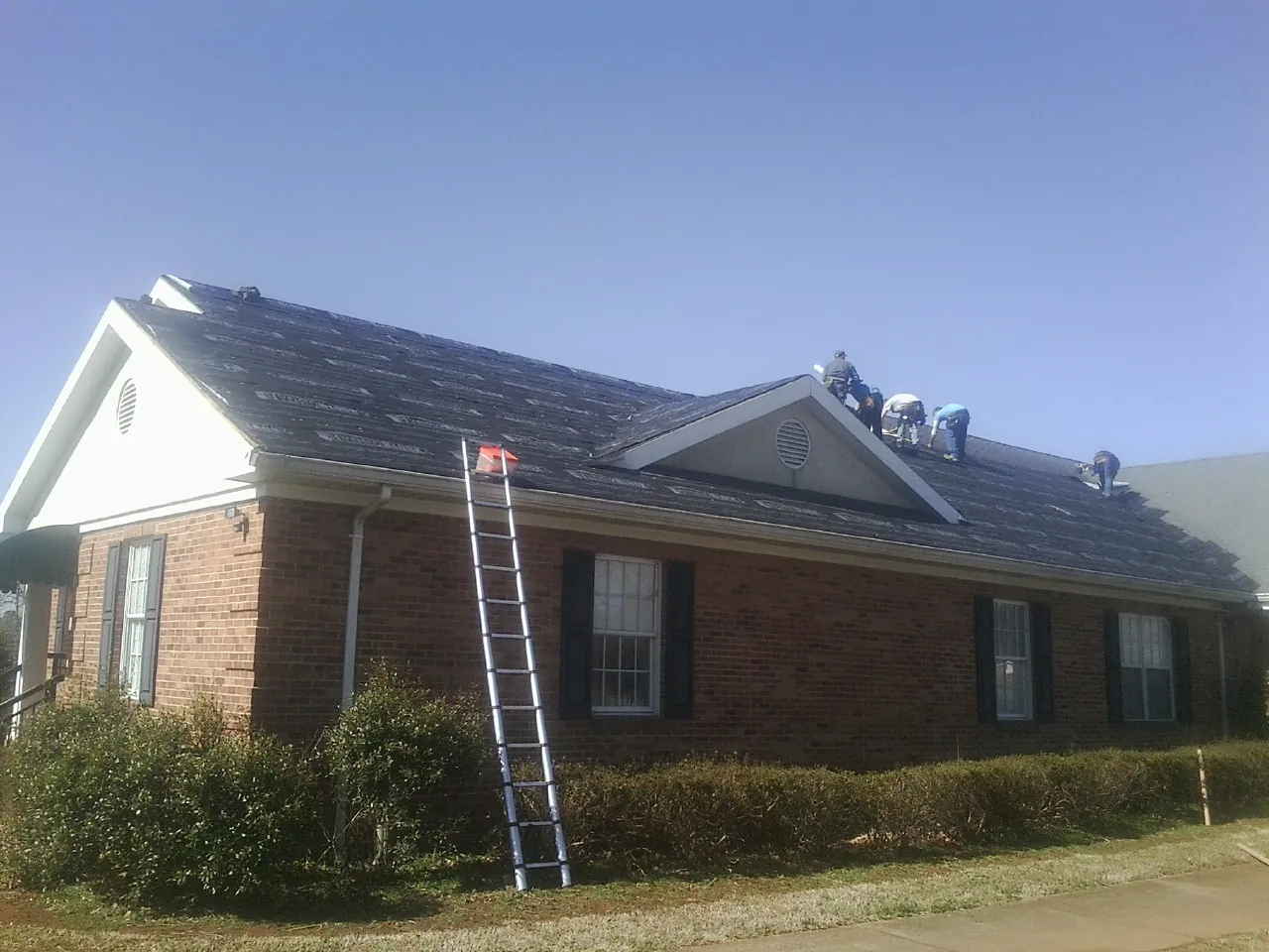 Crew tearing shingles off a brick ranch roof with a ladder set — Emergency Roof Repair work by our crew in Huntingdon