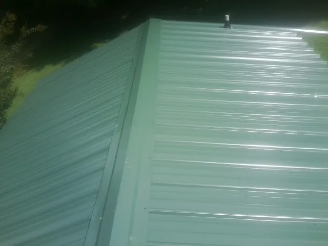 New green metal panels meeting at the ridge of a roof — Flat Roof Repair work by our crew in Huntingdon