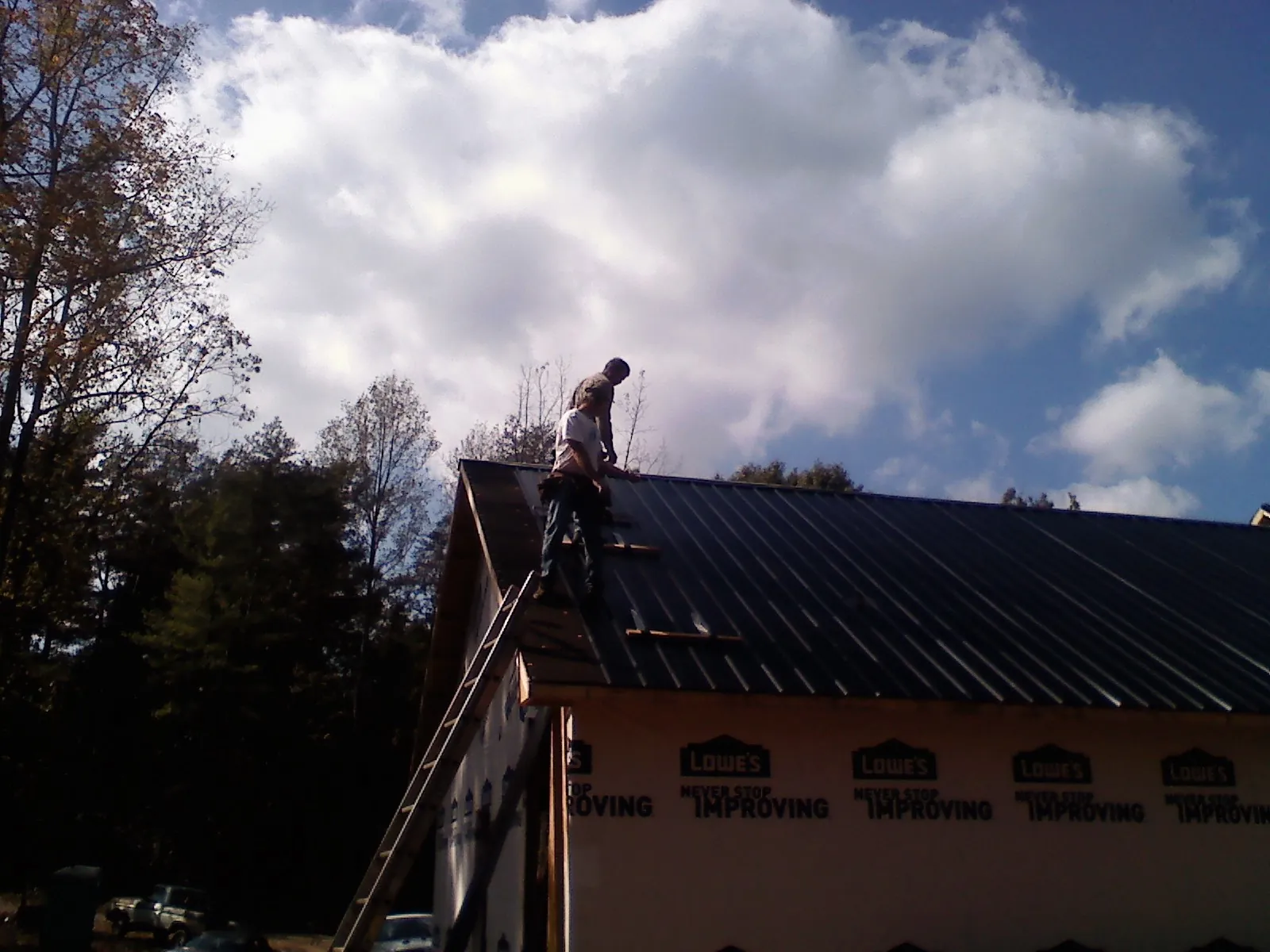 Roofer fastening dark metal panels high against a cloudy sky, from a Roof Inspection job in Huntingdon