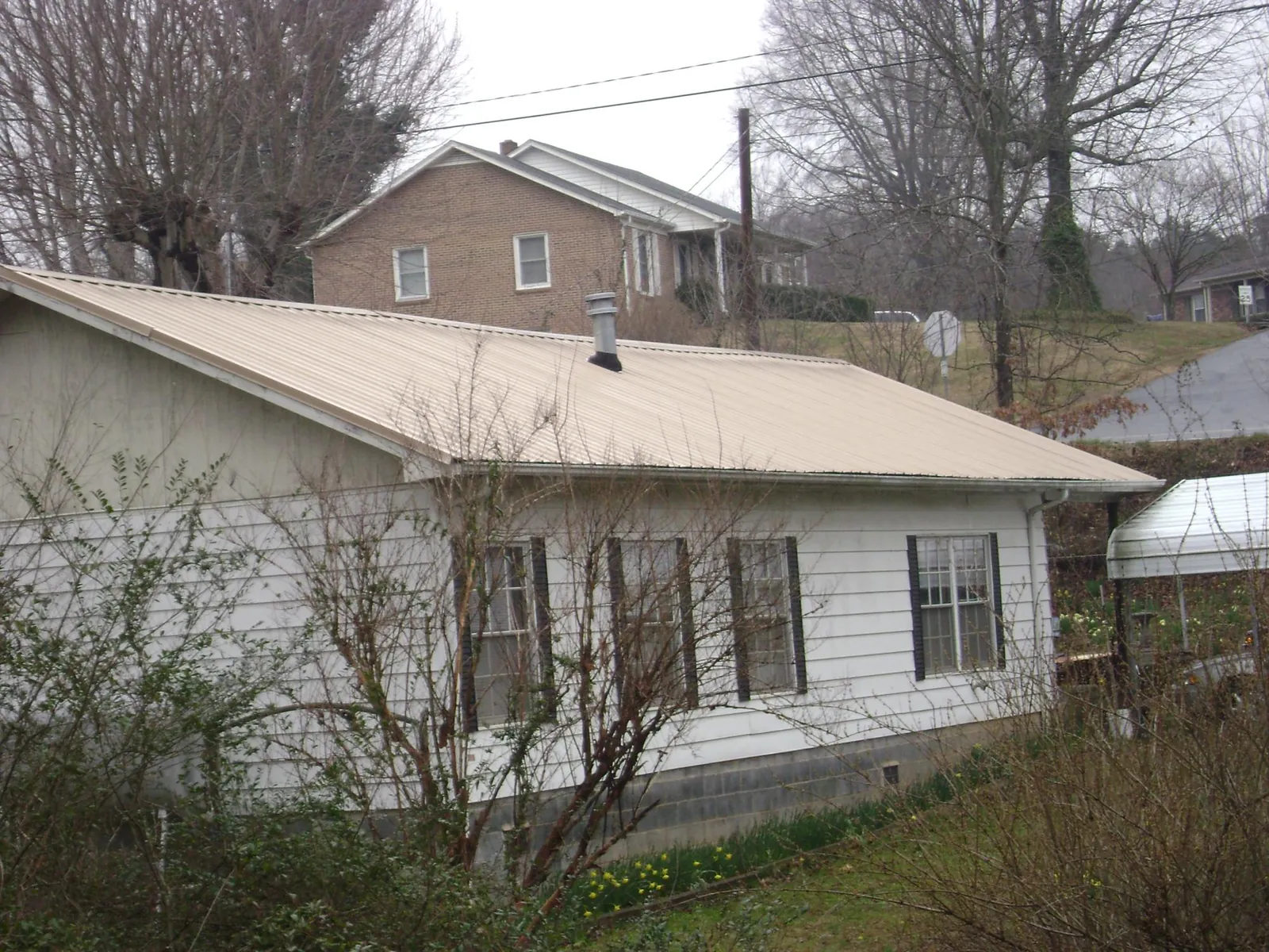 Tan metal roof on a white sided house set into a hillside — Commercial Roofing by Roofing Brothers in Huntingdon